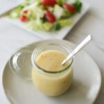 Vinaigrette in a glass container on a plate. Salad with tomatoes on square plate in background
