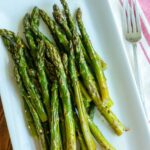 Roasted asparagus on white rectangle dish with a fork next to it