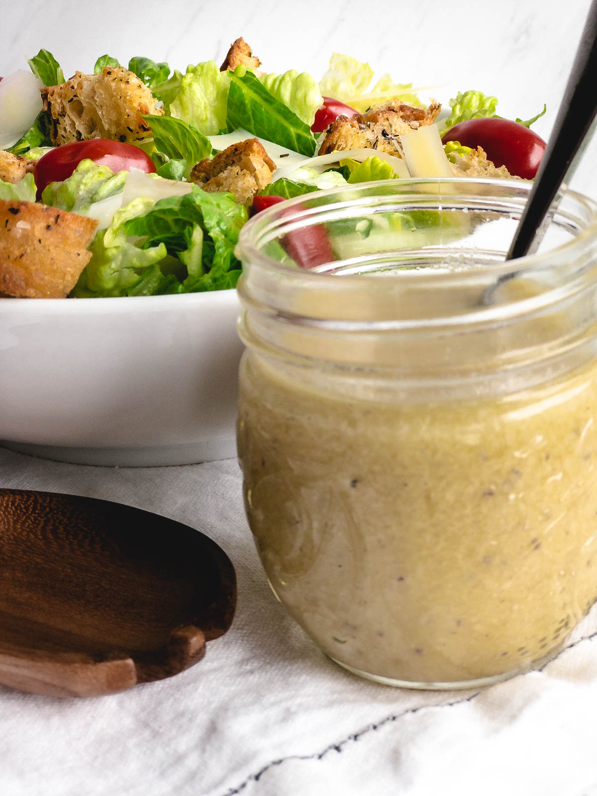 Caesar dressing in a glass jar with a white bowl of salad