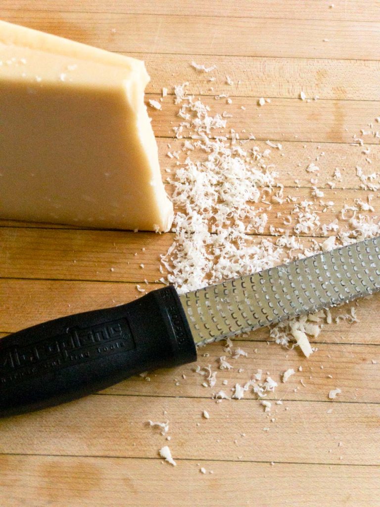 finely grated Parmesan cheese, with a chunk of the cheese and a microplane sitting on a cutting board.
