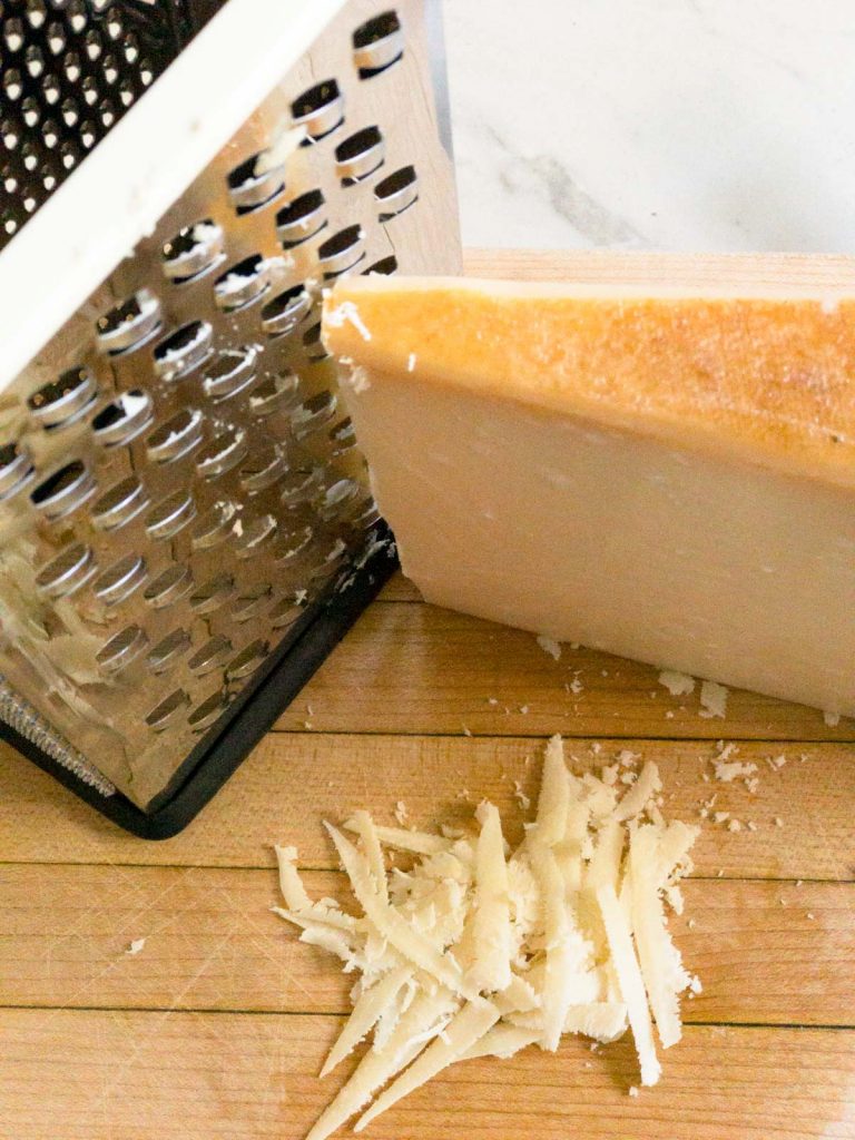box grater with Parmesan cheese and grated cheese next to it on a wood cutting board