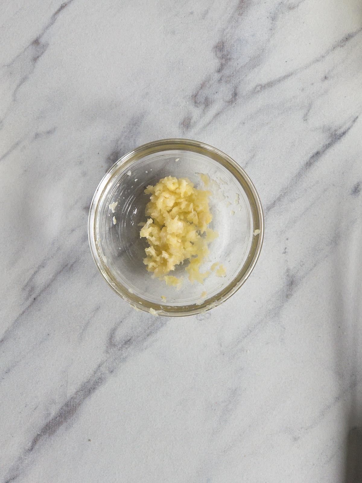 Pressed garlic in a glass bowl on a marble counter