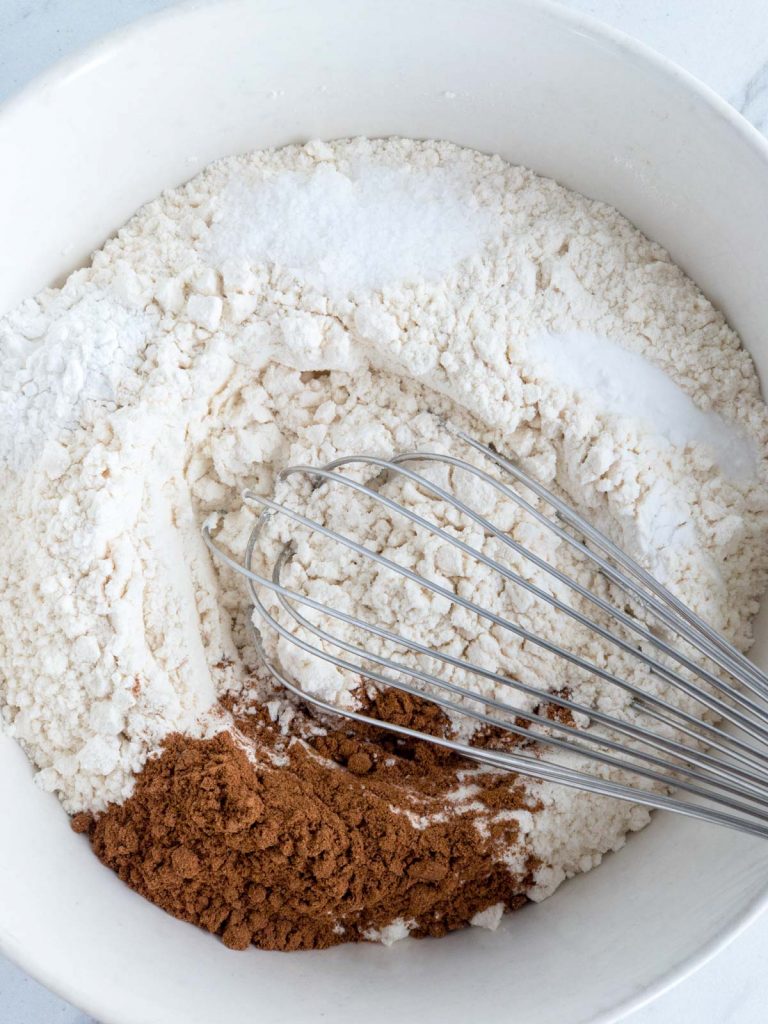 Flour, spices, baking powder & soda and salt in a white bowl with a whisk