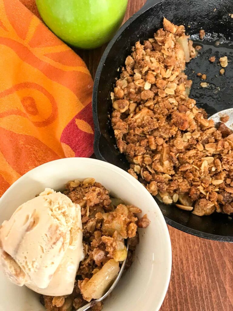 Skillet apple crisp in a cast iron pan and in a white servine bowl with ice cream on top