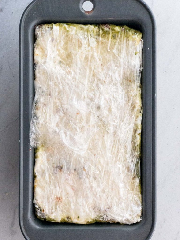 pesto spread in loaf pan covered in plastic wrap
