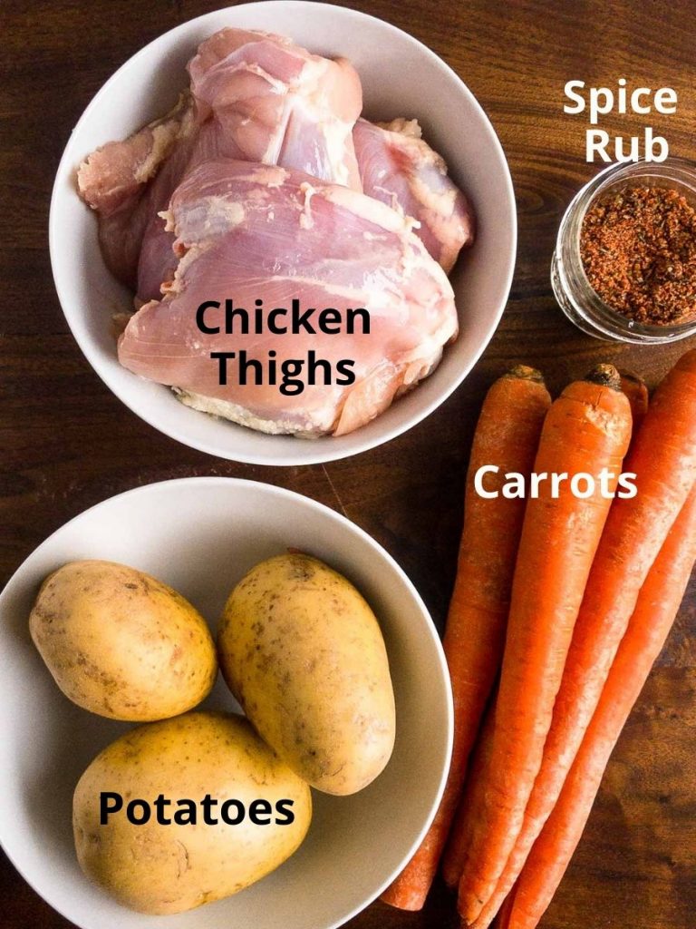 Chicken Thighs in a bowl, spice rub in a glass jar, whole potatoes in a white bowl, 3 whole carrots.  