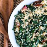 Kale and quinoa salad with tomatoes in a bowl, wood salad tongs next to bowl and lemon above bowl