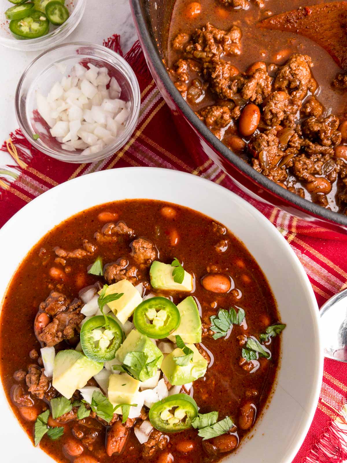 Turkey chili in a white bowl garnished with onions, avocado and jalapeno s