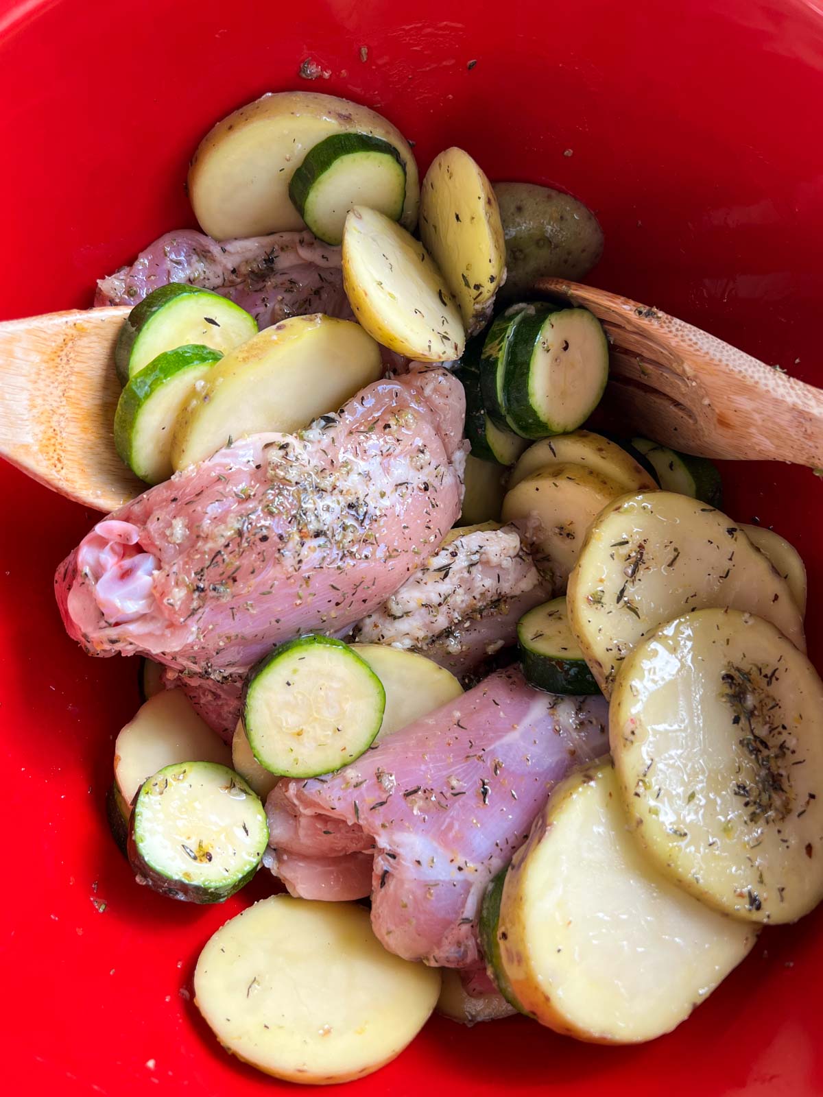 Tossing chicken, potatoes and zucchini with herb oil in a red bowl