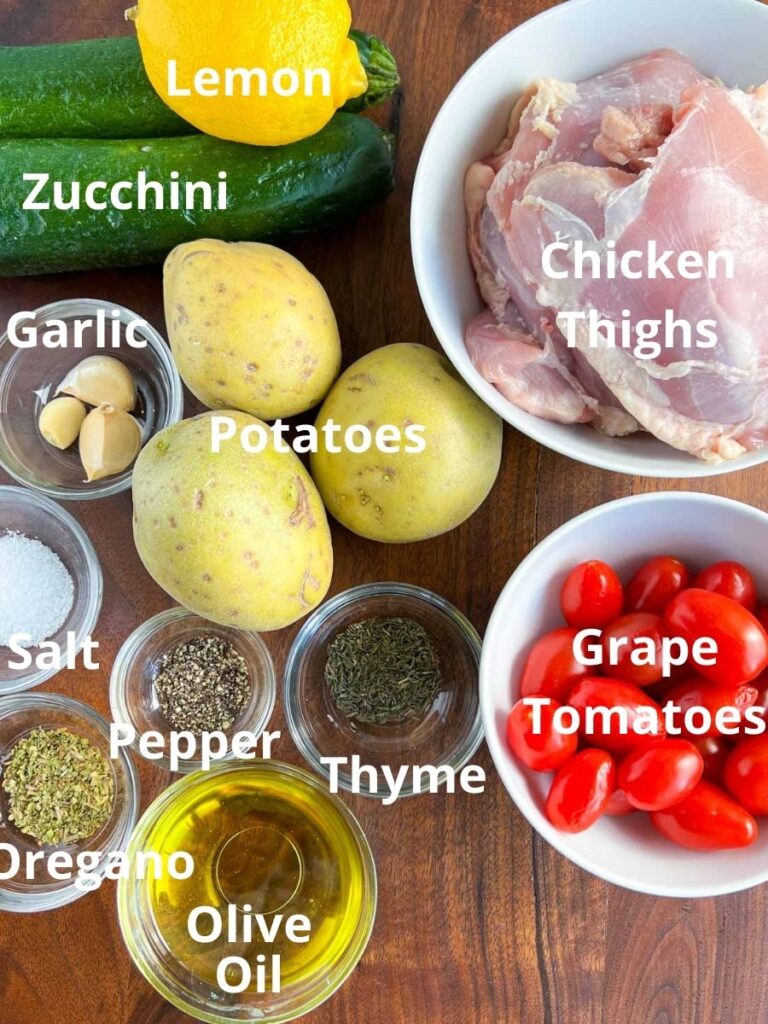 Zucchini, lemon, potatoes, chicken, tomatoes and spices in small bowls on a wood board