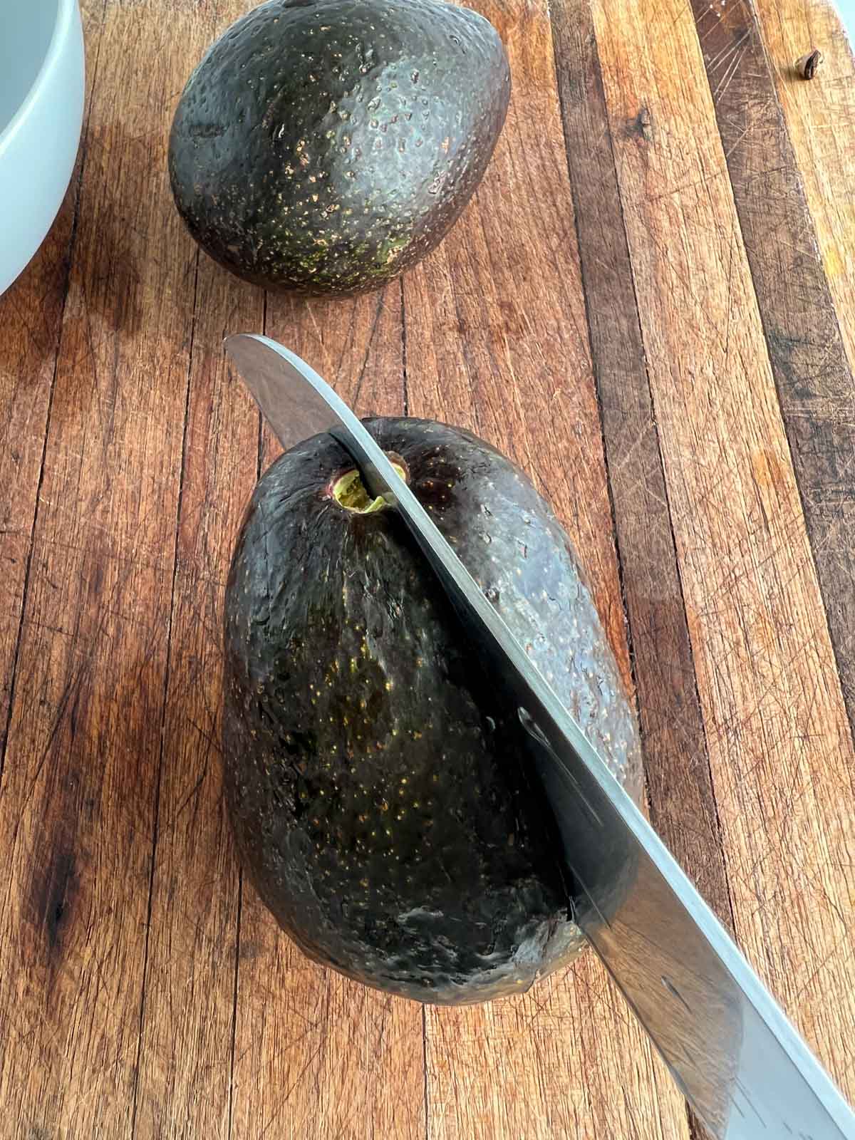 Knife cutting into an avocado on a cutting board