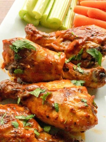 Buffalo Chicken Drumsticks with celery and carrot sticks on a white plate