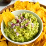 Guacamole in a white bowl surrounded by chips