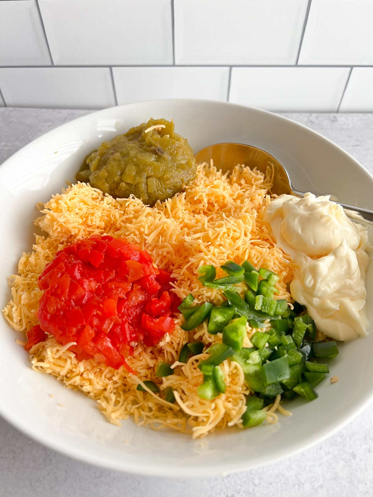 Grated cheddar cheese, pimento, diced chilies, diced jalapeno, mayonnaise in a white bowl