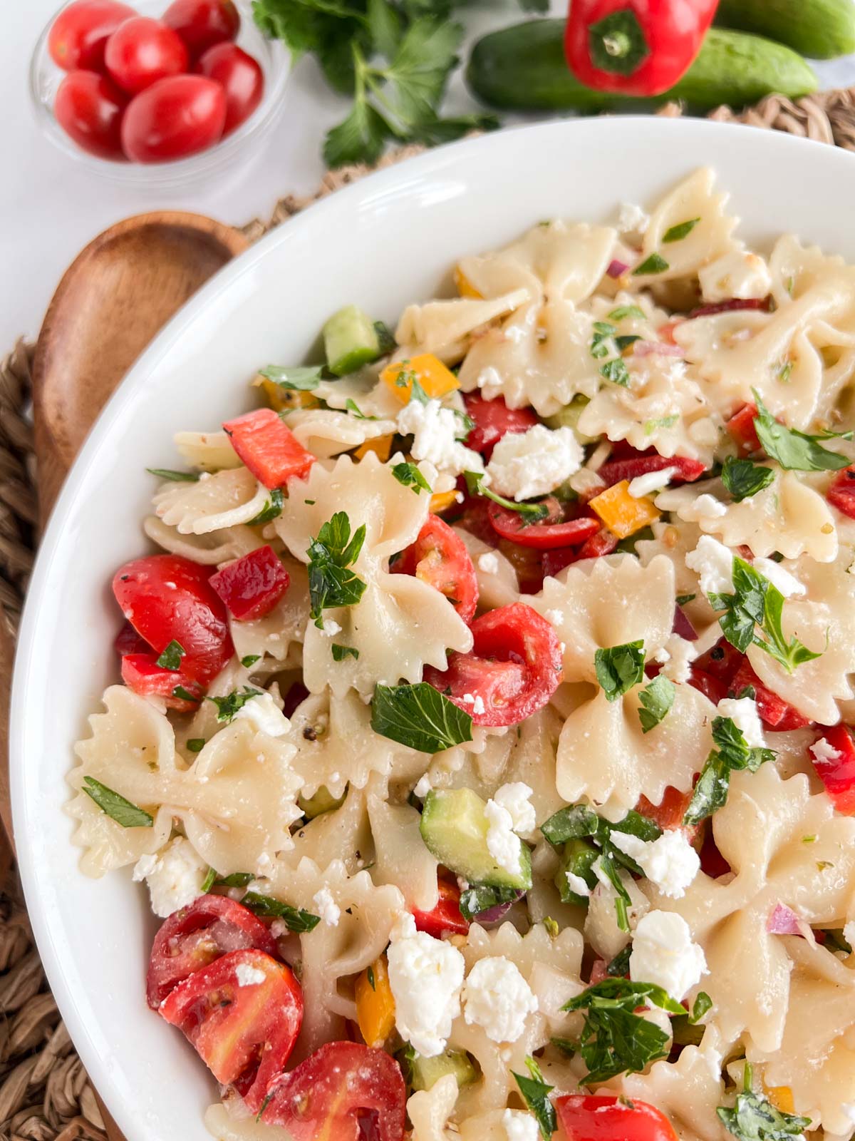 Greek pasta salad in a white bowl, farfalle pasta, cherry tomatoes, parsley, feta cheese, cucmber