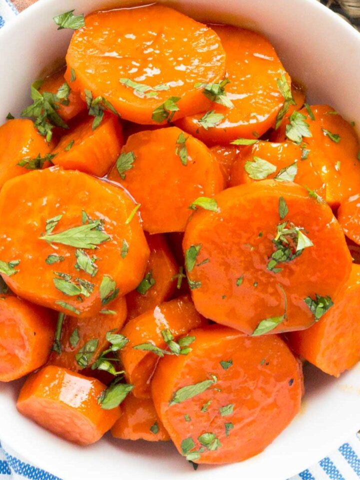 Honey glazed sweet potato slices with parsley garnish in a white bowl