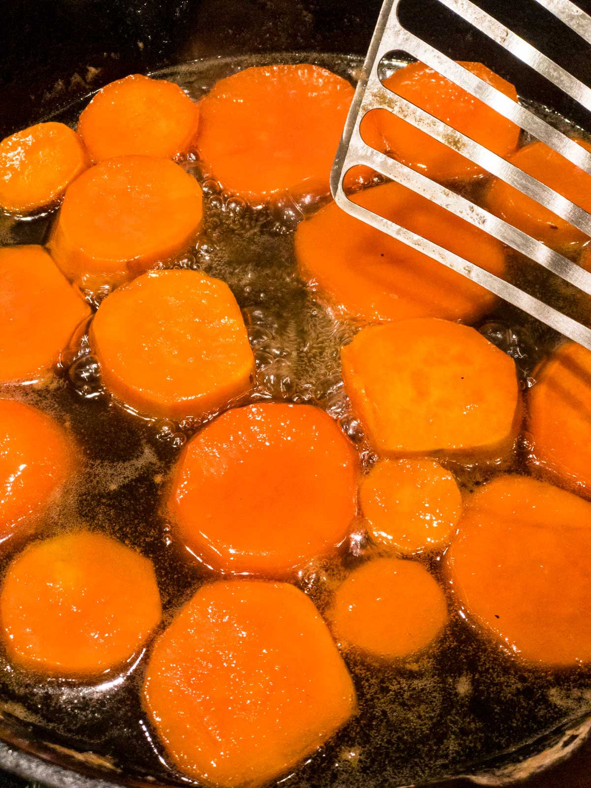 Sweet potato rounds cooking in a cast-iron pan with butter, honey and water