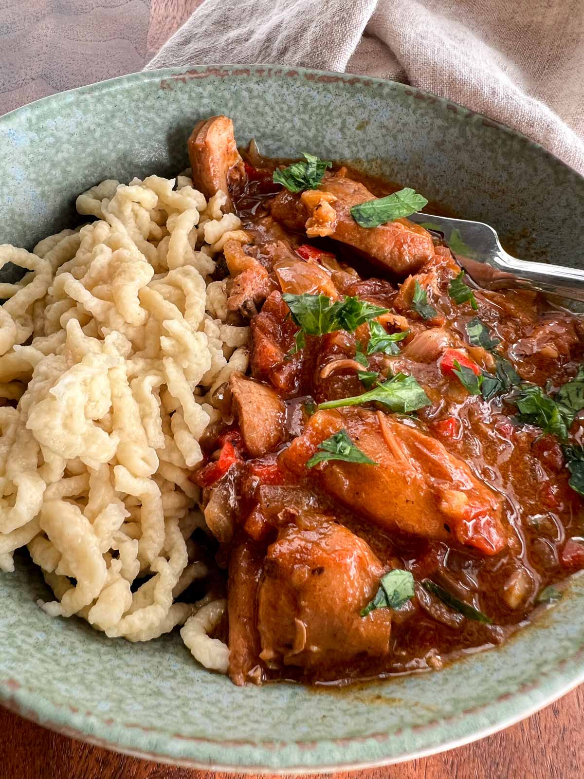 Chicken paprikas and spatsle in greenish colored bowl with a fork on the side