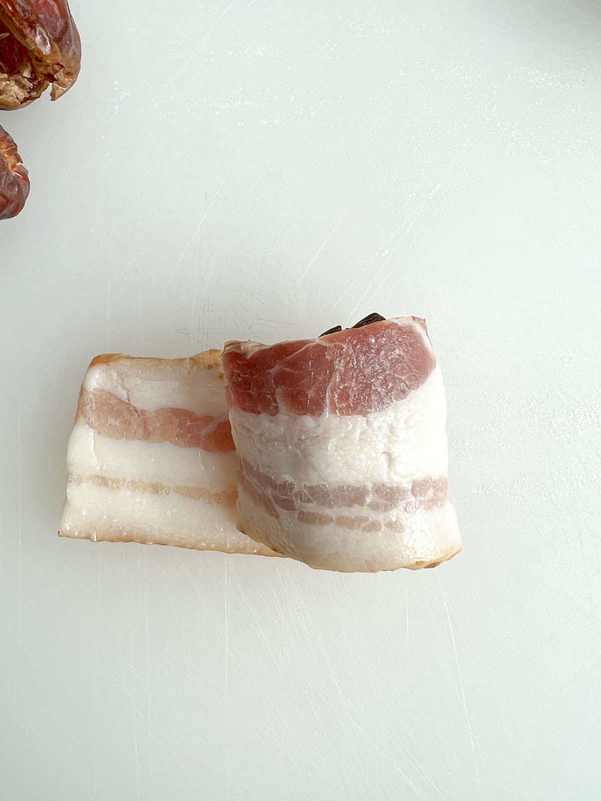 bacon wrapped halfway around a date on a white plastic cutting board