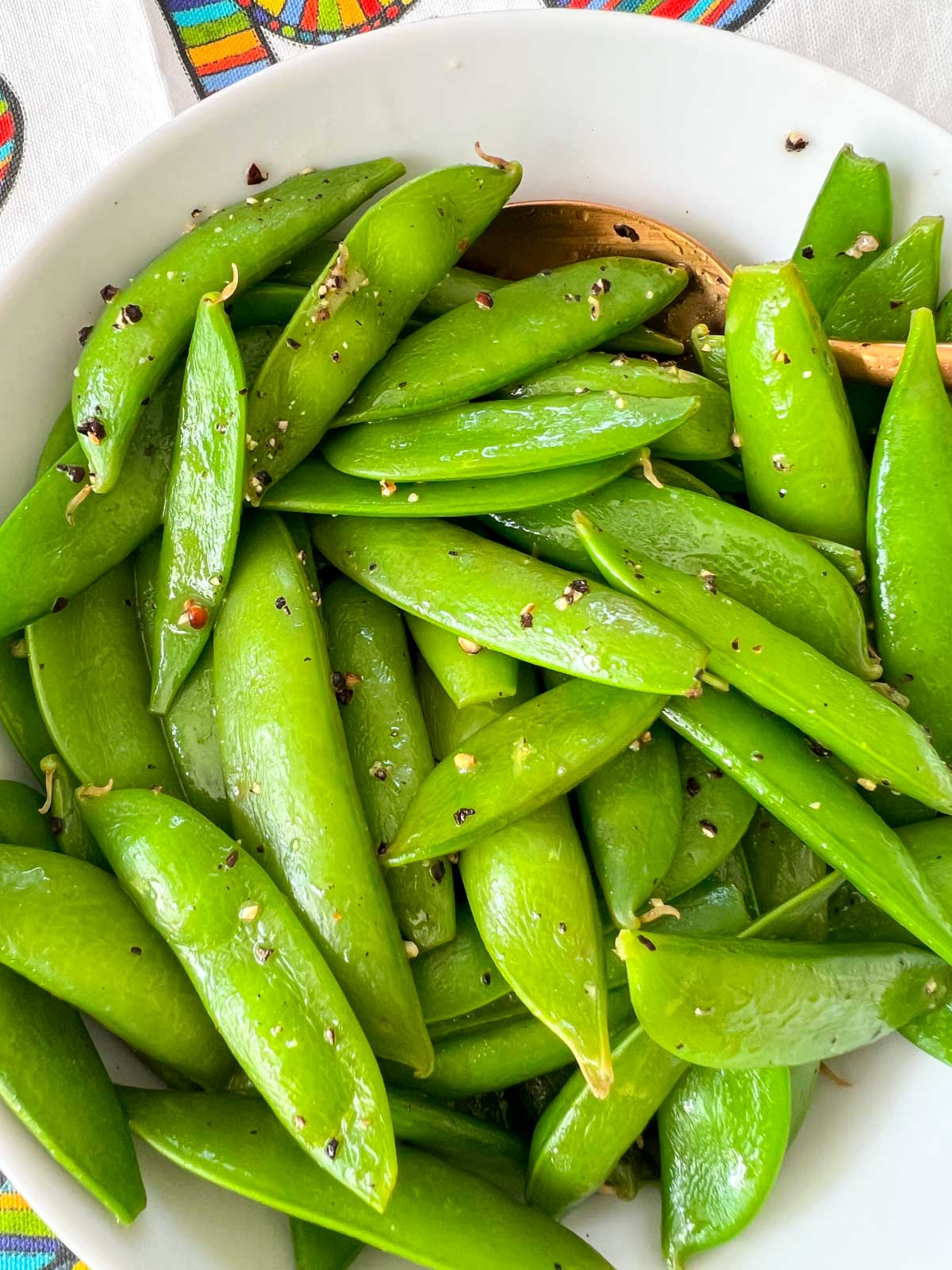 Cooked sugar snap peas in a white bowl seasoned with pepper and salt