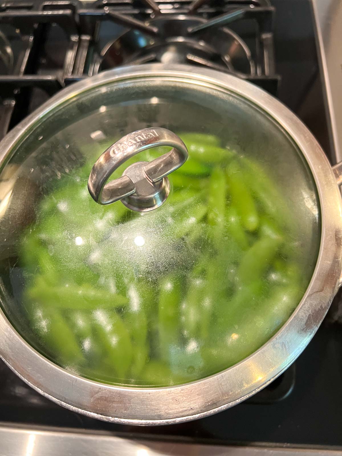 sugar snap peas in a sauce pan that has a clear plastic cover on it