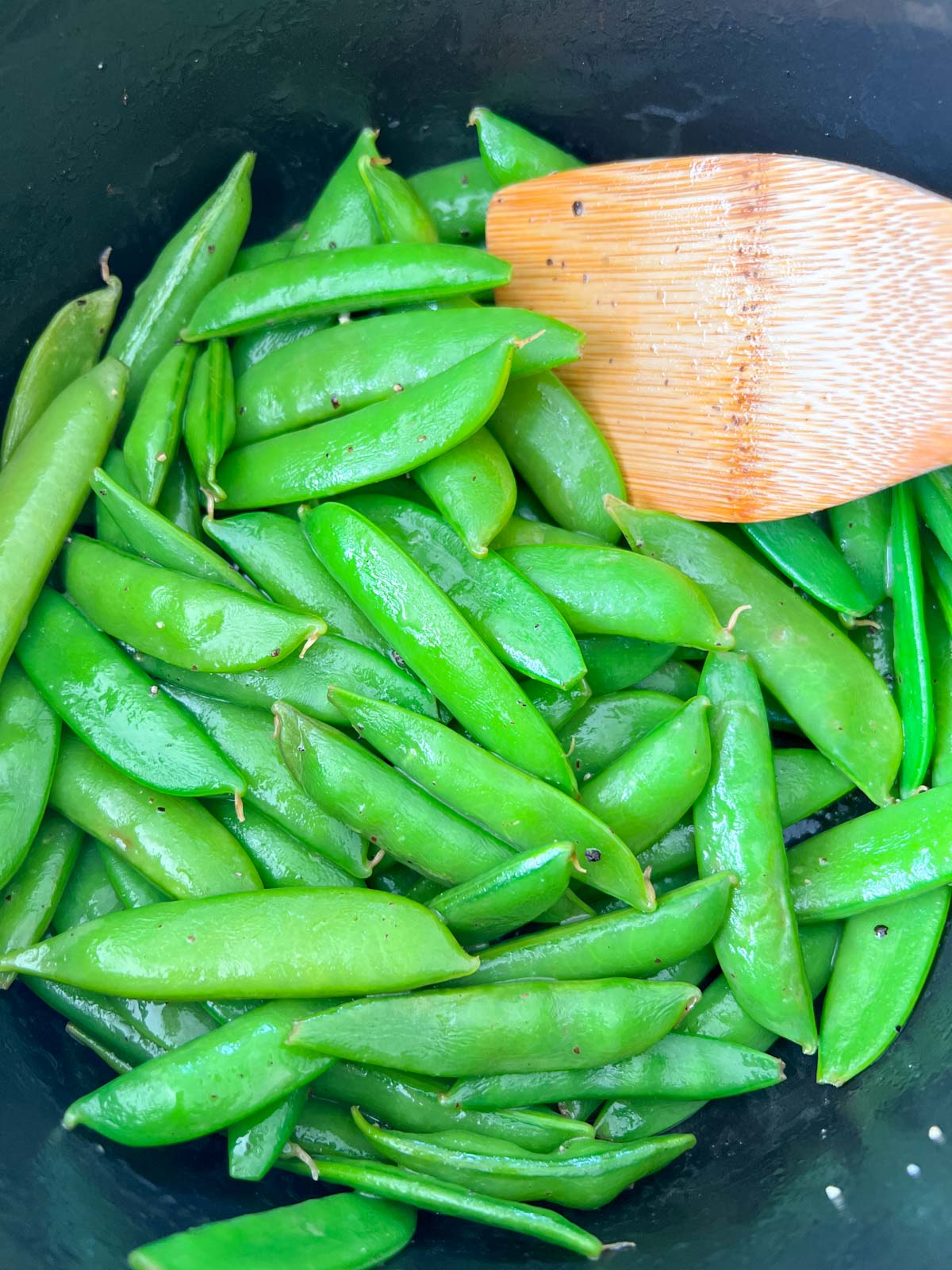 sugar snap peas in a sauce pan with a wooden spoon