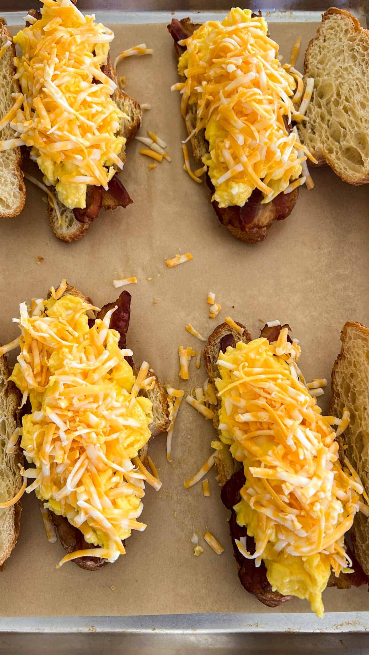 Croissant half layered with bacon on bottom half then scrambled eggs on the bacon and shredded cheese on the eggs