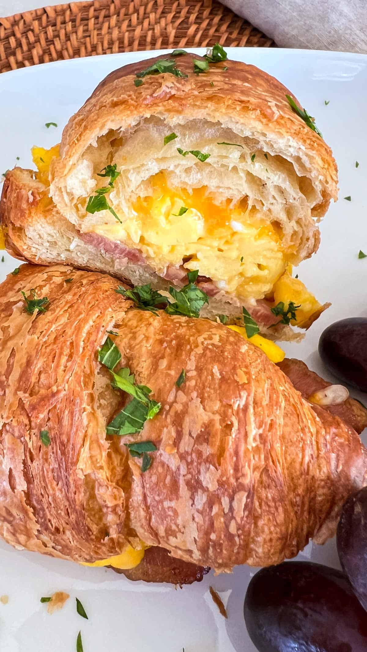 Breakfast Croissant sandwich with scrambled eggs, cheese and bacon cut in half on a white plate with