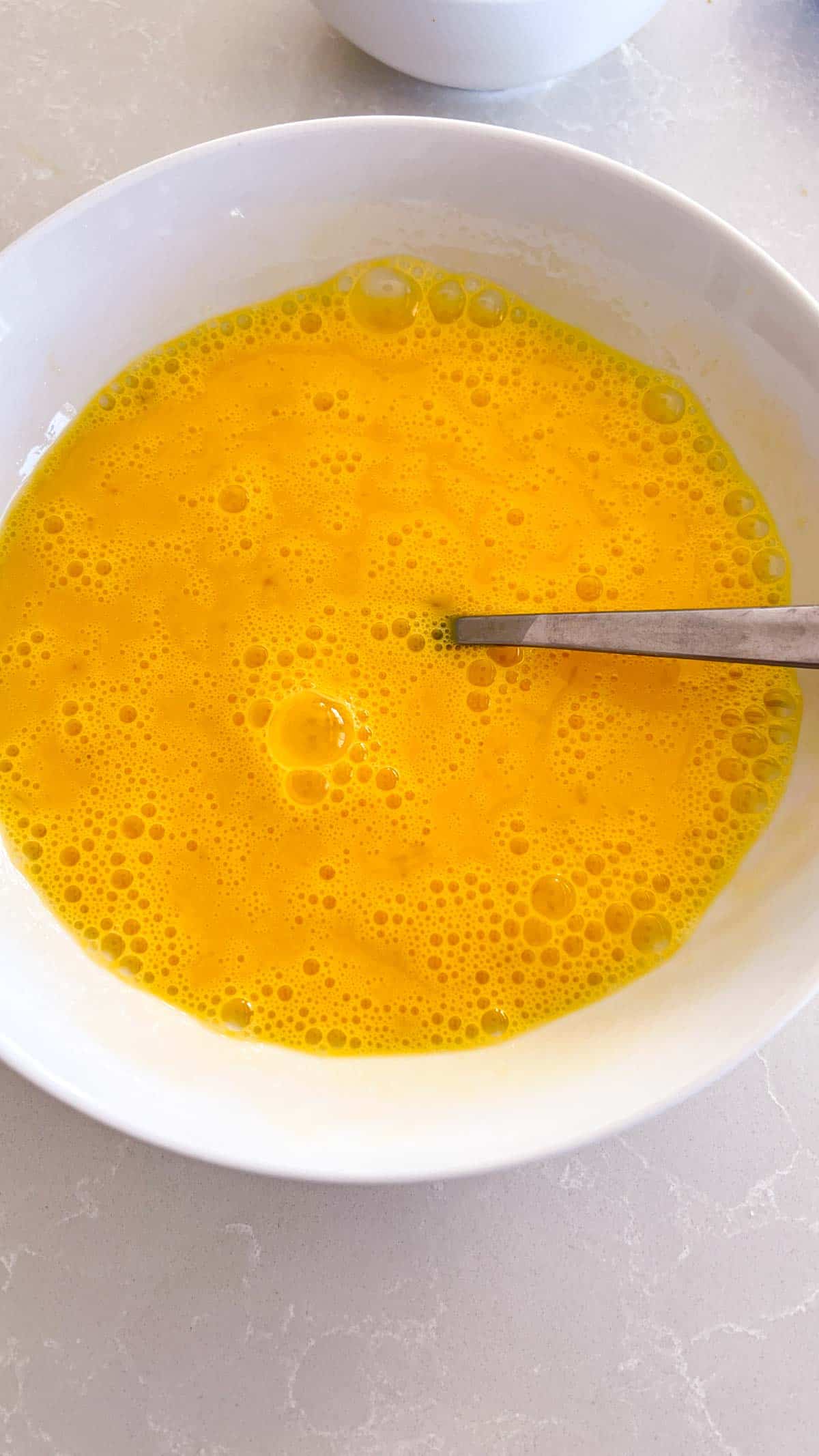 Whisked eggs in a white bowl
