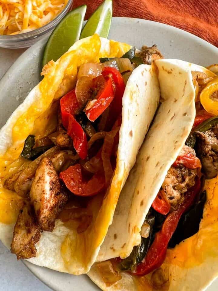 Two chicken fajitas in tortillas on a round plate